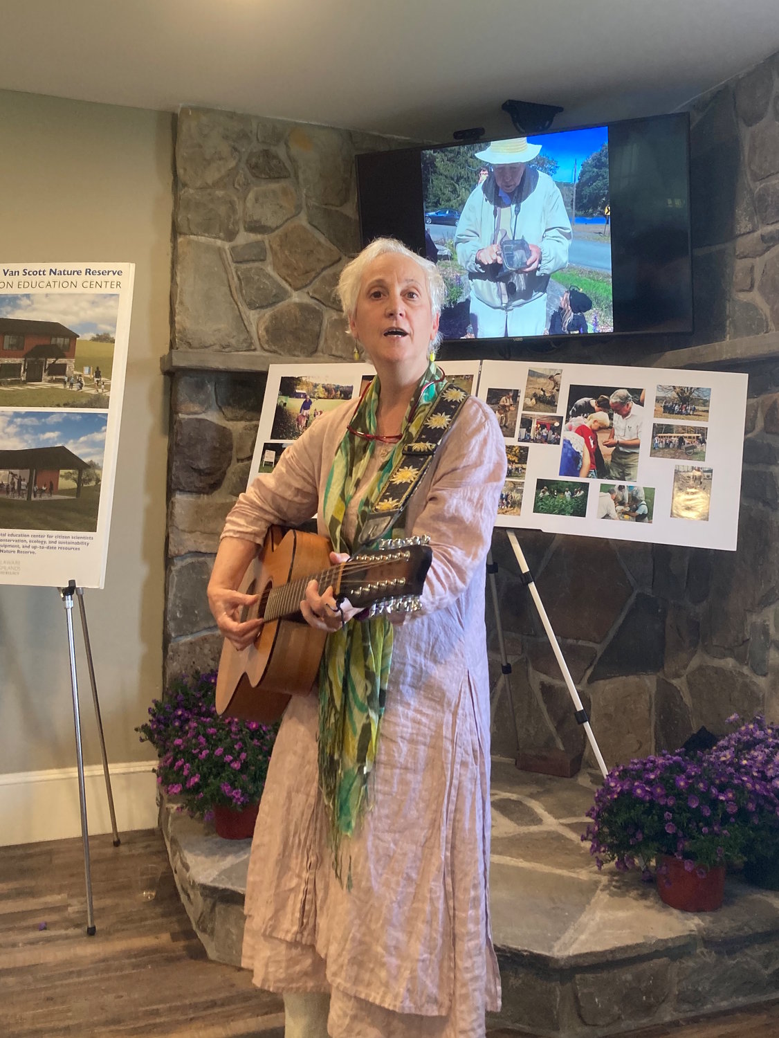 Longtime River Reporter publisher and editor, Rev. Laurie Stuart, shares her musical gifts at a memorial gathering celebrating the life of naturalist Ed Wesely, the founding author of this River Talk column. Wesely appears on the screen behind Stuart.